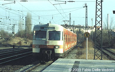 Ankunft vom orange-weißen 420 650-4 um 15:37 Uhr als S 20 (Deisenhofen - München Pasing) (München Hbf 15:25 - Klagenfurt Hbf 20:22) mit 1116 006-6 rauscht durch den Bahnhof Heimeranplatz (München, Frühling 2002).